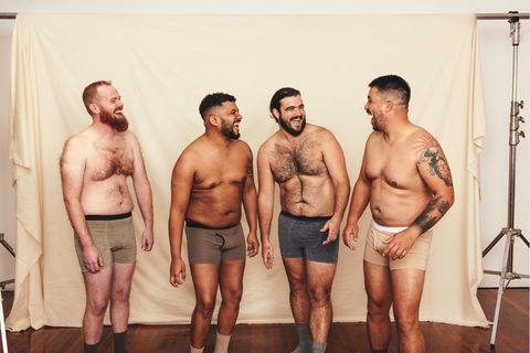 Vier hemdlose Männer lachen fröhlich, während sie vor einem Studiohintergrund stehen