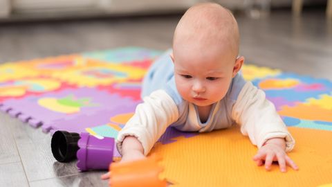 Ein Baby liegt auf einer Spielmatte am Boden