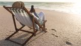 Eine Person liegt mit dem Smartphone in einem Liegestuhl am Strand