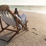 Eine Person liegt mit dem Smartphone in einem Liegestuhl am Strand