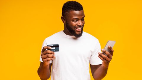 Mann shoppt via Smartphone online und hält Kreditkarte in der Hand