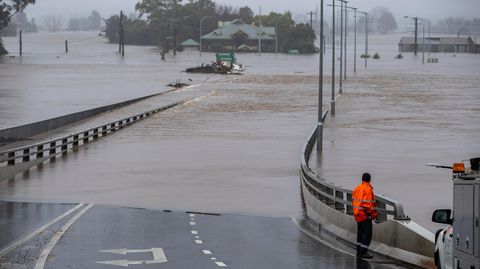 Eine Person in Warnweste steht vor einer überfluteten Straße in Australien.
