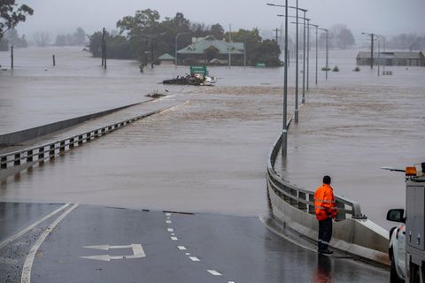 Eine Person in Warnweste steht vor einer überfluteten Straße in Australien.