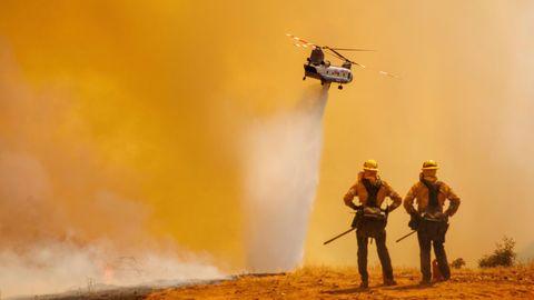 Zwei Einsatzkräfte beobachten einen Chinook-Hubschrauber, der Löschwasser über das "Electra Fire" bei Pine Acres, US-Bundesstaat Kalifornien, abwirft. Das schnell um sich greifende Feuer bedroht mehr als 1200 Gebäude.