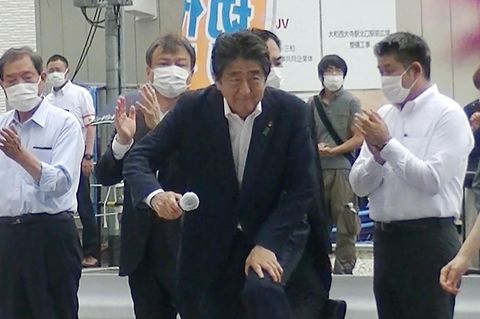 Shinzo Abe betritt die Rednerbühne, dahinter steht der Attentäter