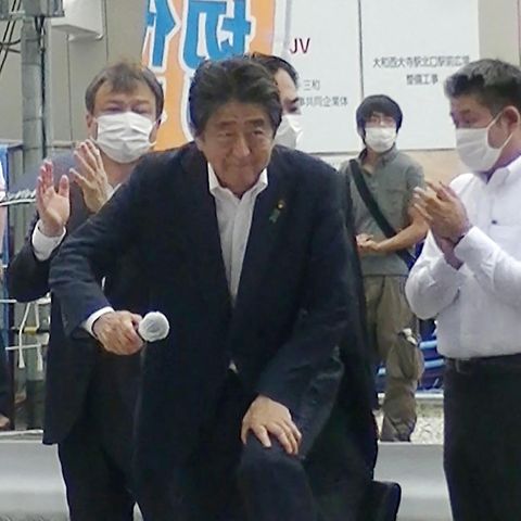 Shinzo Abe betritt die Rednerbühne, dahinter steht der Attentäter