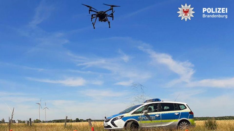 Ein Polizeiauto steht auf einem Feld, darüber eine Drohne
