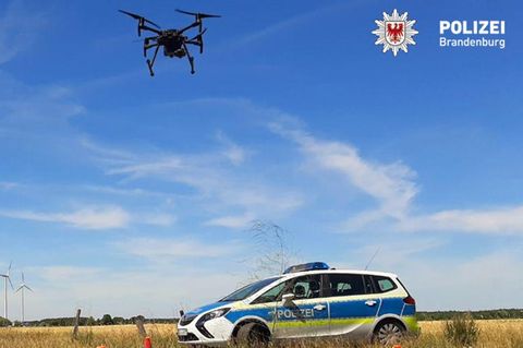 Ein Polizeiauto steht auf einem Feld, darüber eine Drohne