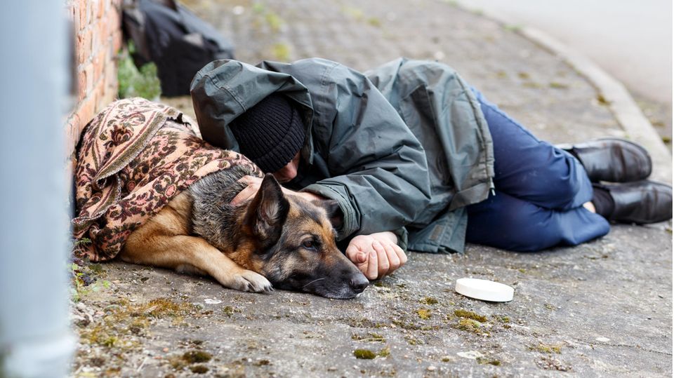 Ein obdachloser Mann und ein Hund liegen auf einen Bürgersteig