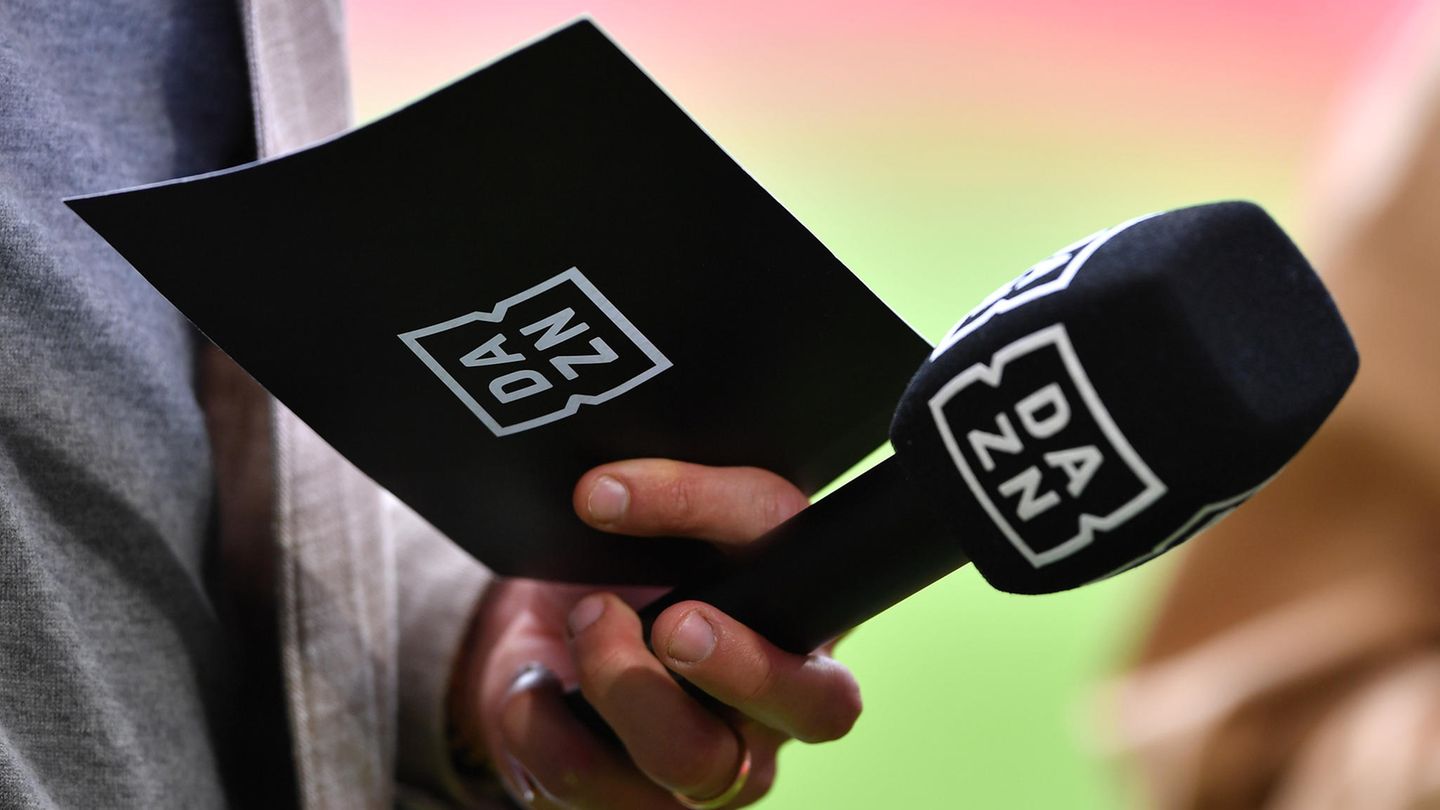 Sport-Reporter hält ein Mikrofon und eine Moderationskarte mit DAZN-Logo in der Hand