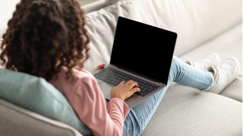Deals und Angebote: Frau sitzt mit einem Laptop auf dem Schoß auf der Couch