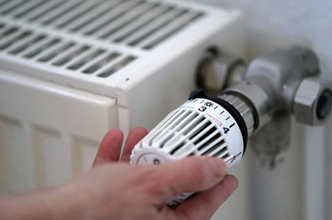 Eine Frau dreht an einem Heizungsthermostat