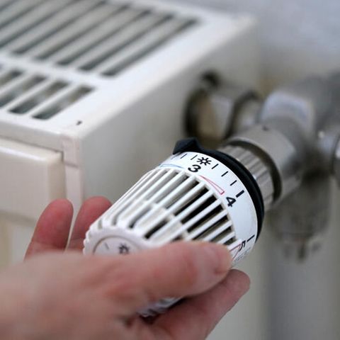 Eine Frau dreht an einem Heizungsthermostat