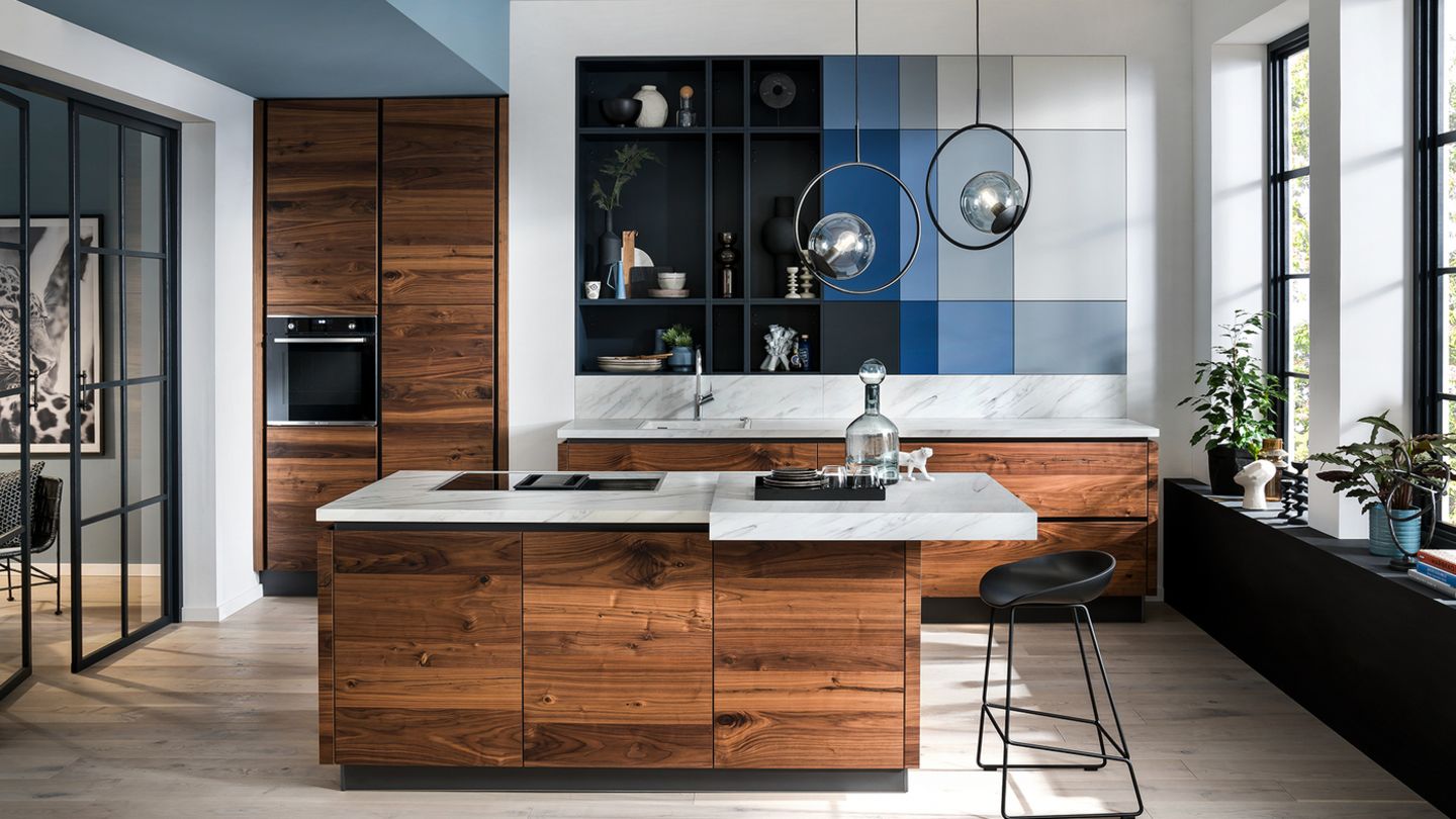 Und ewig lockt das Holz  Ein ewiger Trend, auch 2022: Küchenfronten aus Holz. Keine Bange mit den muffigen Landhausstil haben die modernen Holzküchen nichts mehr gemein, sie kommen minimalistisch, luftig und sehr edel daher. Kombiniert wird die Holzküche gern mit Marmor, Beton oder Edelstahl. Holz verströmet immer den Charme von Individualität. Schließlich sind die natürlichen Hölzer, allen voran Nussholz,  immer in Sachen Maserung und Farbton immer Unikate. Größter Vorteil der Holzküche: Sie kommen nie aus der Mode. Gut gepflegt setzen sie über die Jahre eher würdevolle Patina an.