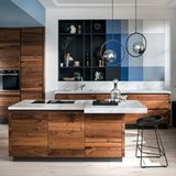 Und ewig lockt das Holz  Ein ewiger Trend, auch 2022: Küchenfronten aus Holz. Keine Bange mit den muffigen Landhausstil haben die modernen Holzküchen nichts mehr gemein, sie kommen minimalistisch, luftig und sehr edel daher. Kombiniert wird die Holzküche gern mit Marmor, Beton oder Edelstahl. Holz verströmet immer den Charme von Individualität. Schließlich sind die natürlichen Hölzer, allen voran Nussholz,  immer in Sachen Maserung und Farbton immer Unikate. Größter Vorteil der Holzküche: Sie kommen nie aus der Mode. Gut gepflegt setzen sie über die Jahre eher würdevolle Patina an.