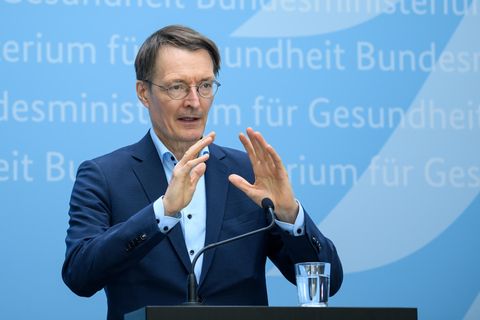 Karl Lauterbach gestikuliert vor blauem Hintergrund