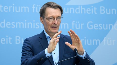Karl Lauterbach gestikuliert vor blauem Hintergrund