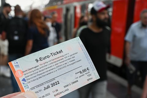 9 Euro Ticket in einer Hand vor Szene mit Fahrgästen der Bahn