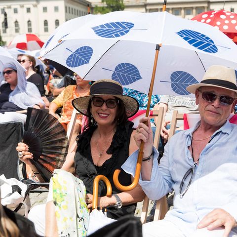 Menschen mit Sonnenhut und Schirm auf Platz