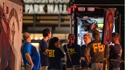 Vor einer Mall stehen Männer und Frauen in "FBI"-T-Shirts hinter einem von innen beleuchteten Kastenwagen