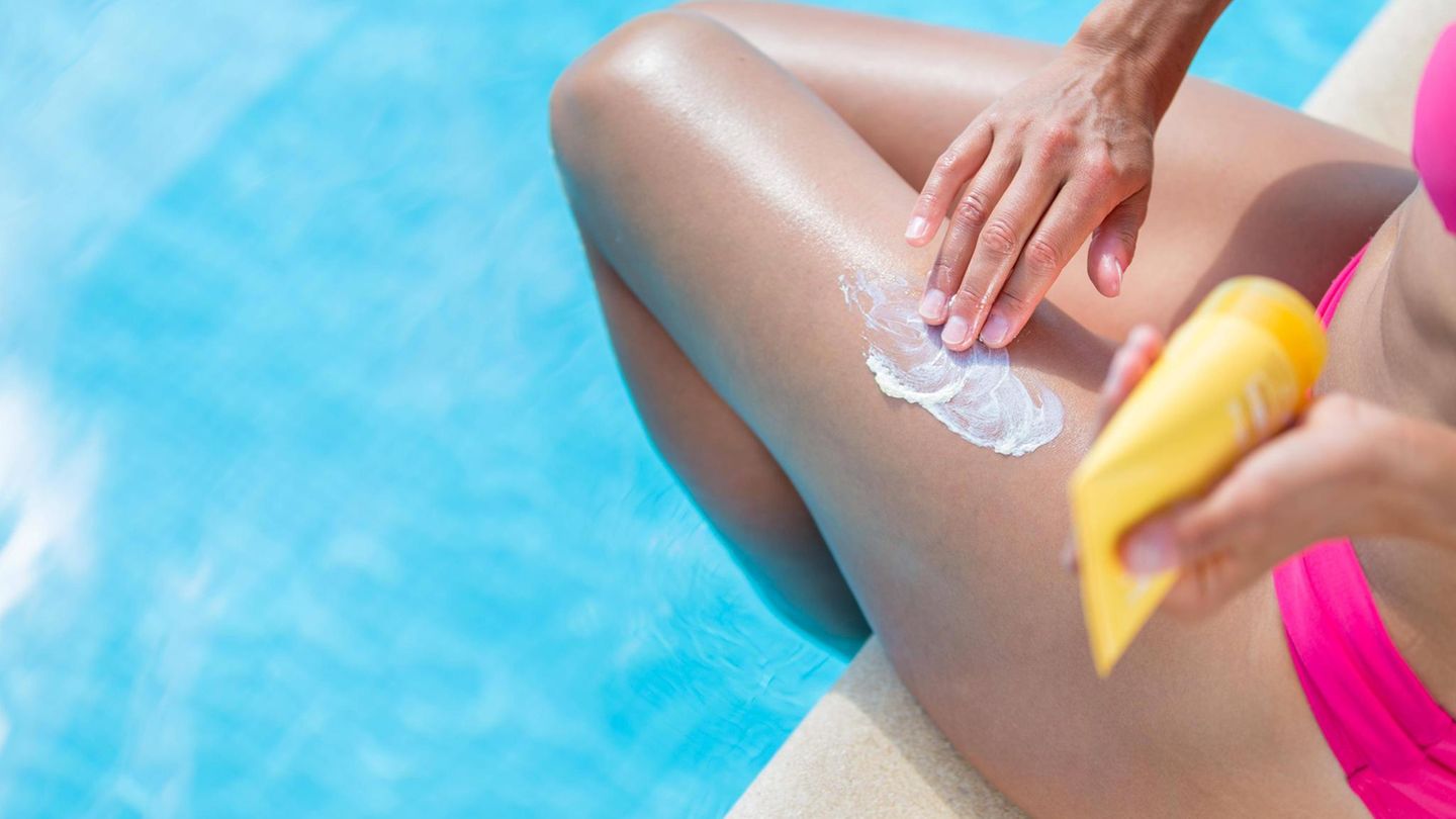 Eine Frau sitzt am Pool und cremt ihr Bein mit Sonnencreme ein