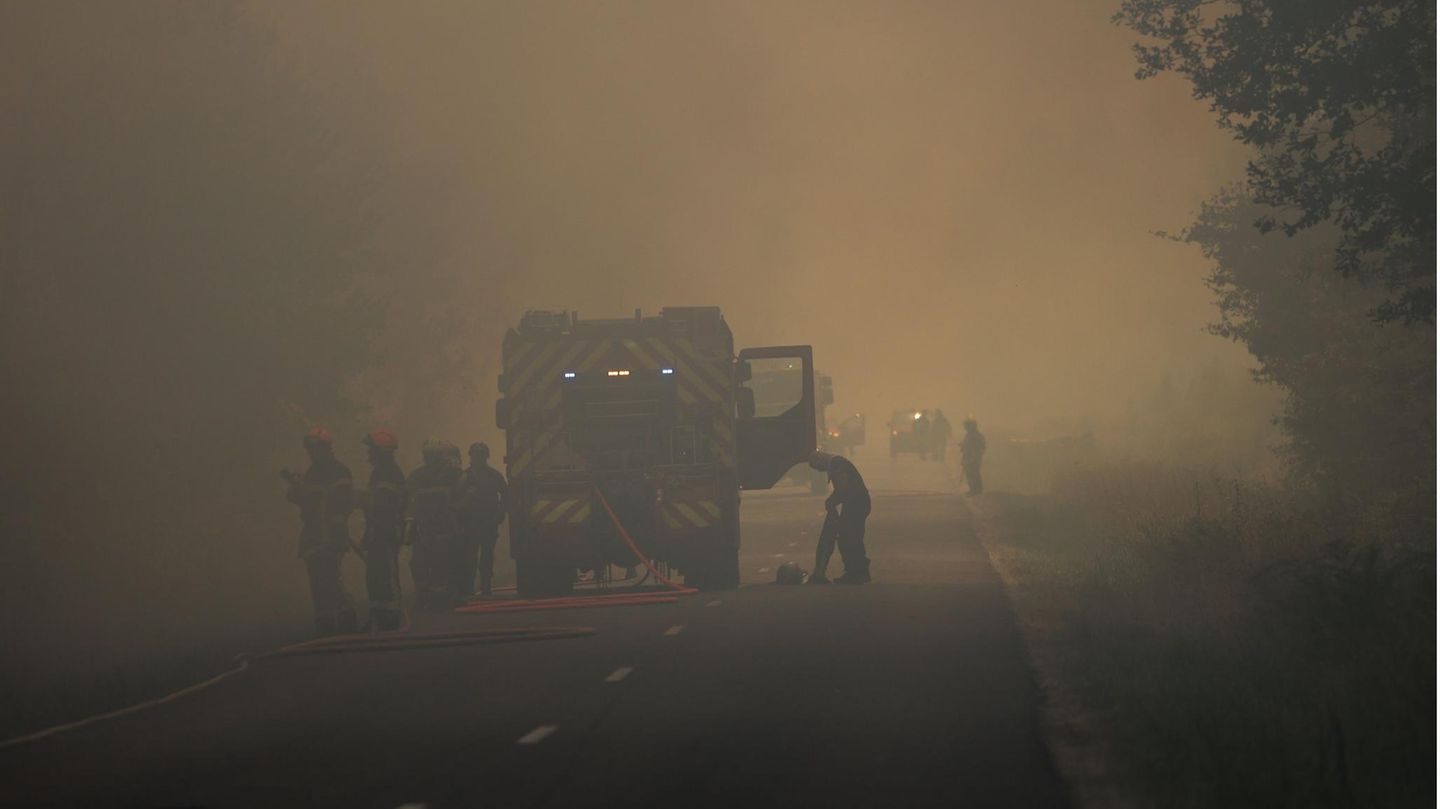 Feuerwehrleute stehen bei Löscharbeiten auf einer Straße in Louchats, Region Gironde, im Südwesten Frankreichs mitten im Rauch