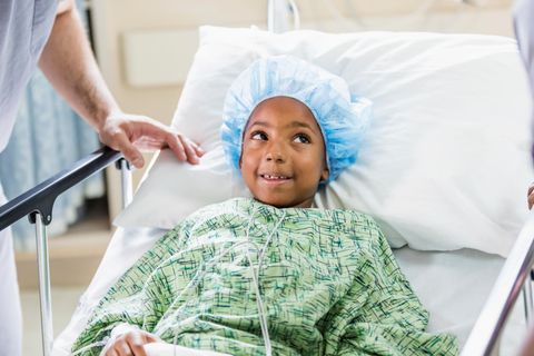 Ein kleiner Junge mit OP-Haube und Mantel im Krankenhausbett