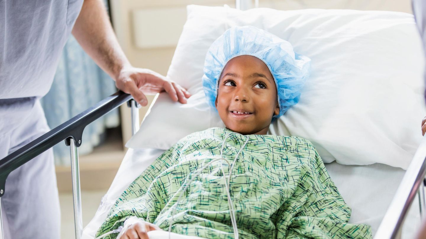 Ein kleiner Junge mit OP-Haube und Mantel im Krankenhausbett