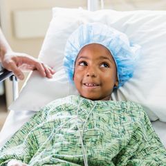 Ein kleiner Junge mit OP-Haube und Mantel im Krankenhausbett