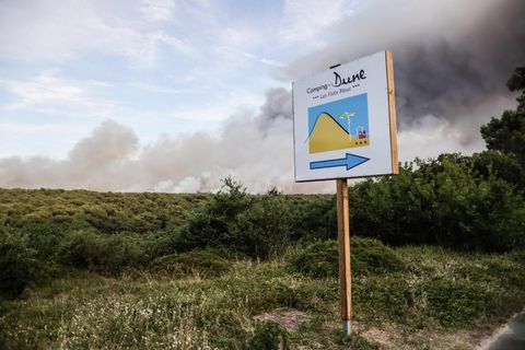 Ein quadratisches, weißes Schild mit blauem Pfeil steckt im Sand und weist den Weg zu einem Camping an der Dune de Pilat