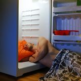 Mann liegt im Kühlschrank