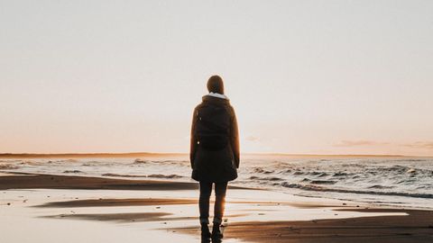 Eine Frau steht beim Sonnenuntergang am Meer.