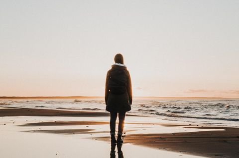 Eine Frau steht beim Sonnenuntergang am Meer.