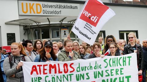Frauen und Männer stehen mit einem Banner "Atemlos durch unsere Schicht, Ihr gönnt uns unsere Pause nicht vor einem Krankenhaus