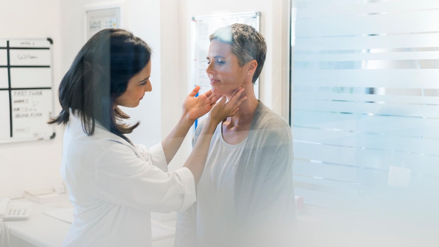 Eine Ärztin tastet die Schilddrüse einer Patientin ab Eine Ärztin tastet die Schilddrüse einer Patientin ab