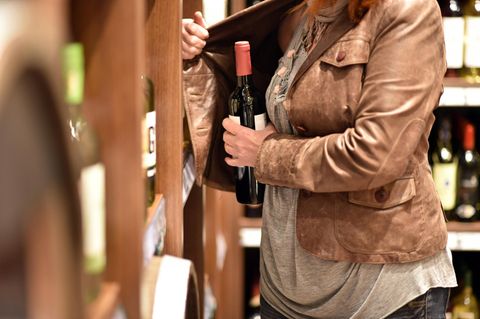 Frau stiehlt eine Flasche Wein und versteckt sie in der Jacke