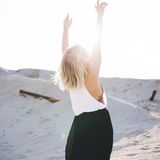 Eine Frau streckt bei Sonnenschein am Strand ihre Hände in die Luft.