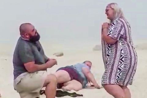 Ein Mann macht einer Frau einen Heiratsantrag am Strand – ihre Schwester stürzt im Hintergrund.