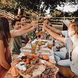 Junge Männer und Frauen sitzen gemeinsam am Esstisch und stoßen an.