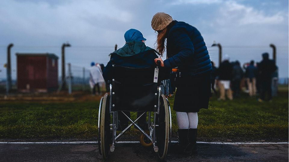 Eine Frau steht mit einem Mann im Rollstuhl am Straßenrand.