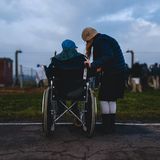 Eine Frau steht mit einem Mann im Rollstuhl am Straßenrand.