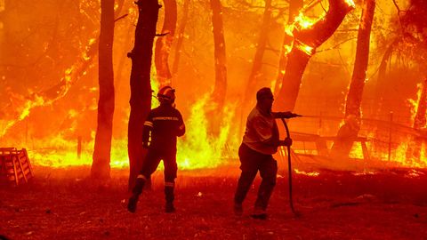 Ein Feuerwehrmann und ein Freiwilliger versuchen Flammen eines Waldbrandes zu löschen