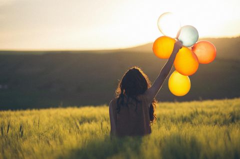 Eine Frau steht auf einer Wiese und hält Luftballons in die Luft.