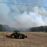 Ein Traktor steht Montag auf einem Acker bei Gransee, während aus dem Wald Rauchwolken aufsteigen