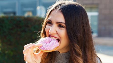 Frau beißt einen Donut ab und erfreut sich am Essen