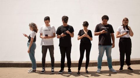 Jugendliche stehen mit ihrem Smartphone in einer Reihe.
