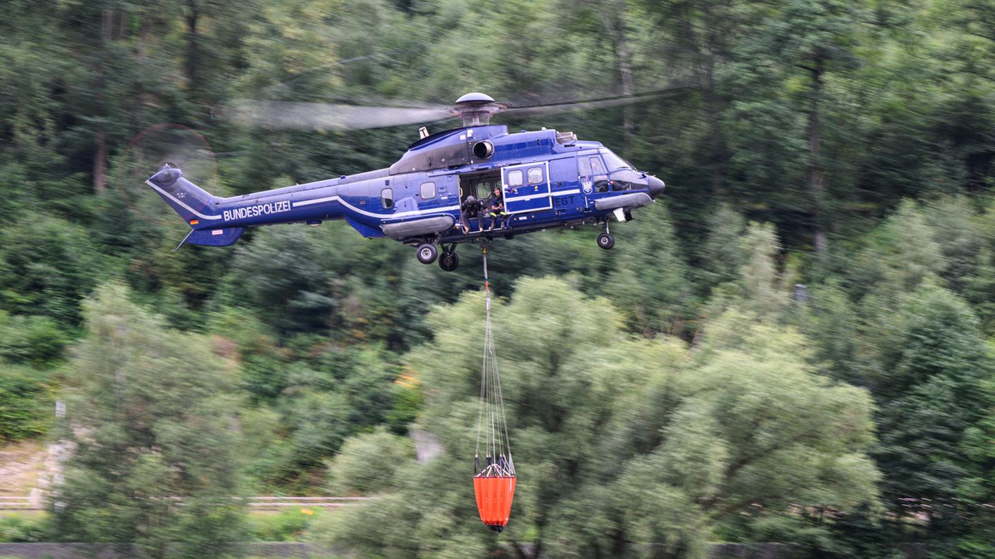 Ein blauer Hubschrauber mit Bundespolizei-Aufschrift fliegt mit orangem Löschsack unter dem Rumpf über einen Wald