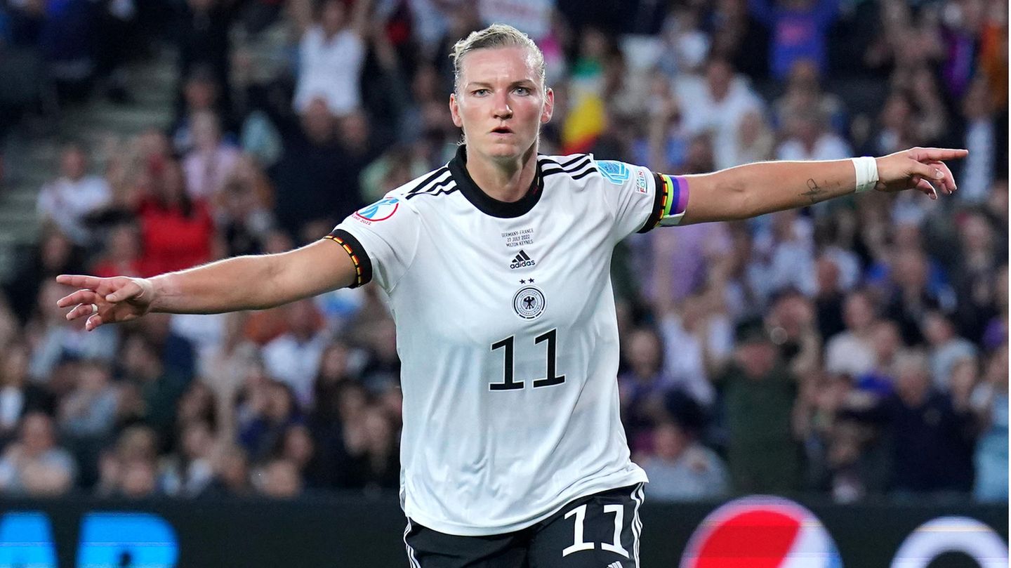 Eine weiße Fußballerin mit blonden Haaren läuft mit ausgebreiteten Armen über den Platz. Sie trägt ein weißes Trikot