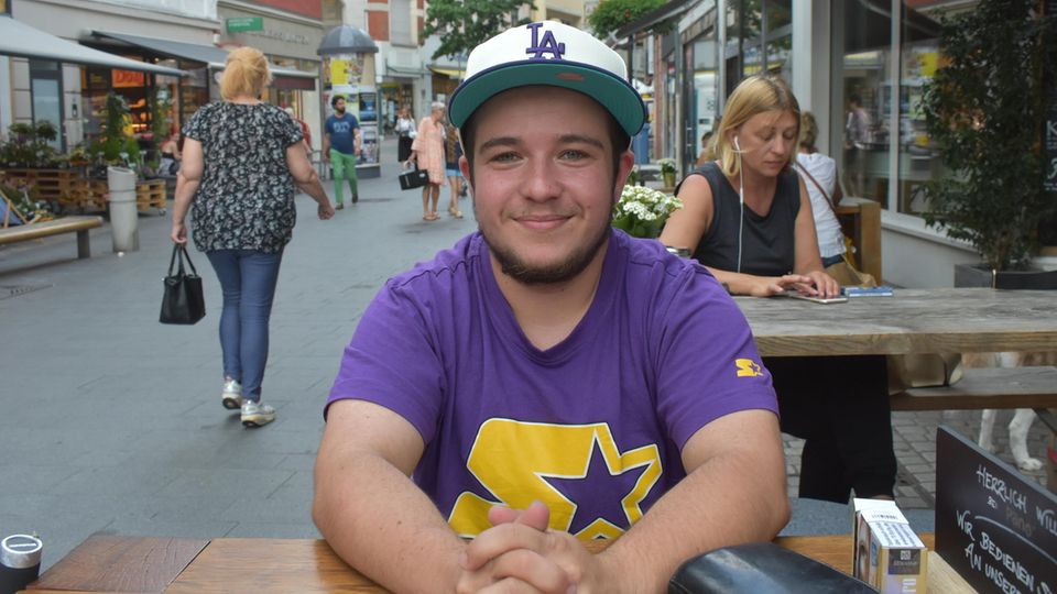 Sebastian sitzt an einem Tisch und lächelt in die Kamera