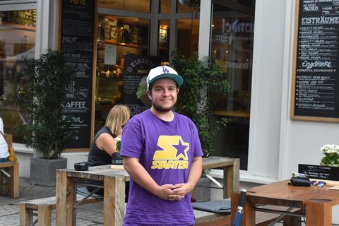 Sebastian steht auf der Straße vor einem Café